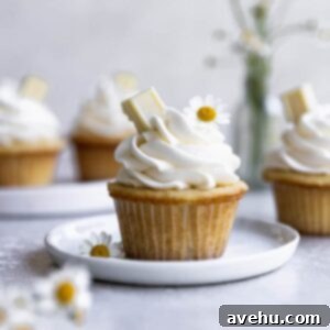 Cloud-Like White Chocolate Cupcakes 2 A white chocolate cupcake on a white plate surrounded by white flowers.