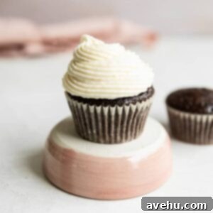 A cupcake on a pink pedestal on a gray surface, adorned with silky Russian buttercream frosting.