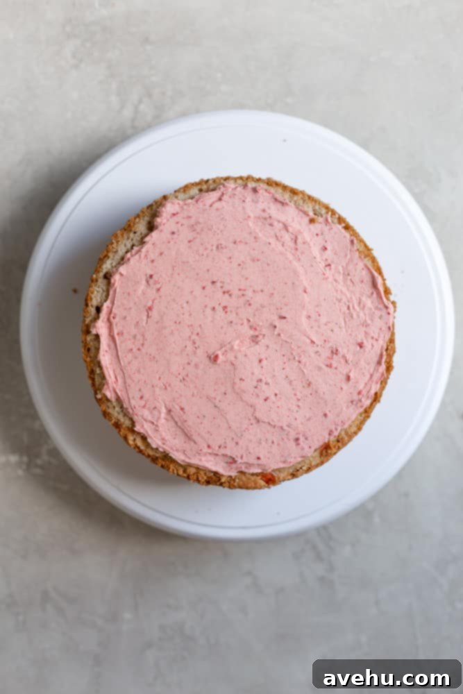 Aromatic Strawberry Basil Cake with Strawberry Buttercream 13 A neatly frosted yellow cake layer adorned with a thick, smooth layer of pink strawberry buttercream.