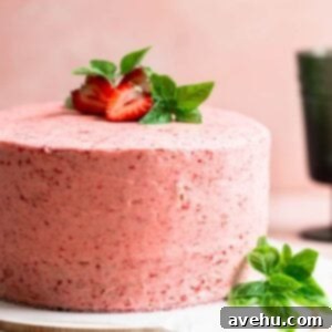 Aromatic Strawberry Basil Cake with Strawberry Buttercream 15 A luscious pink frosted layer cake, adorned with fresh strawberries and basil leaves, on a serving plate.