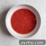 Aromatic Strawberry Basil Cake with Strawberry Buttercream 16 A vibrant red puree, made from fresh strawberries and basil, sits in a white bowl.