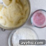 Aromatic Strawberry Basil Cake with Strawberry Buttercream 17 Creamy cake batter in a mixing bowl beside bowls of flour and a vibrant strawberry-milk mixture on a gray background.