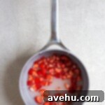 Aromatic Strawberry Basil Cake with Strawberry Buttercream 20 A small saucepan on a stovetop, filled with fresh chopped strawberries, sugar, and water, simmering to create a flavorful simple syrup.