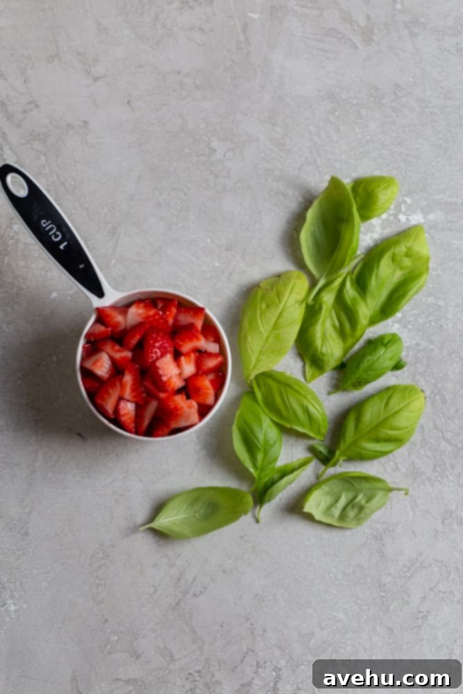 Aromatic Strawberry Basil Cake with Strawberry Buttercream 3 Freshly chopped red strawberries in a measuring cup, accompanied by vibrant green basil leaves, set against a muted gray background.