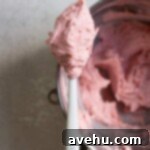 Aromatic Strawberry Basil Cake with Strawberry Buttercream 22 A spatula holding up a swirl of vibrant strawberry pink buttercream, showcasing its smooth and airy texture.