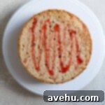 Aromatic Strawberry Basil Cake with Strawberry Buttercream 23 A flat yellow cake layer, generously drizzled with red strawberry simple syrup, ready for the next step of assembly.