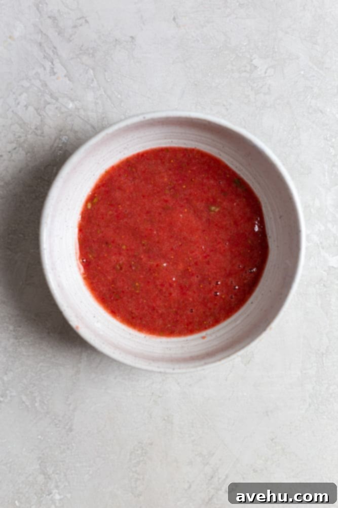 Aromatic Strawberry Basil Cake with Strawberry Buttercream 4 A smooth, vibrant red puree, made from fresh strawberries and basil, sits in a pristine white bowl, ready for cake batter.