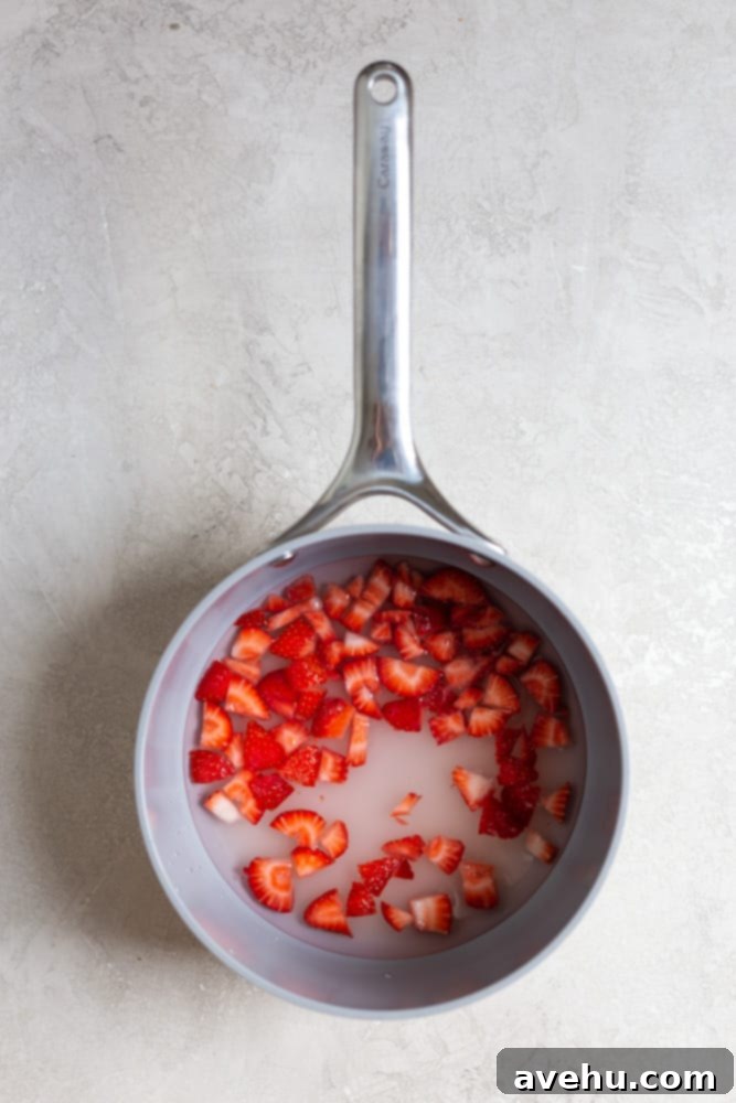 Aromatic Strawberry Basil Cake with Strawberry Buttercream 7 A small saucepan on a stovetop, filled with fresh chopped strawberries and water, simmering to create a flavorful simple syrup.
