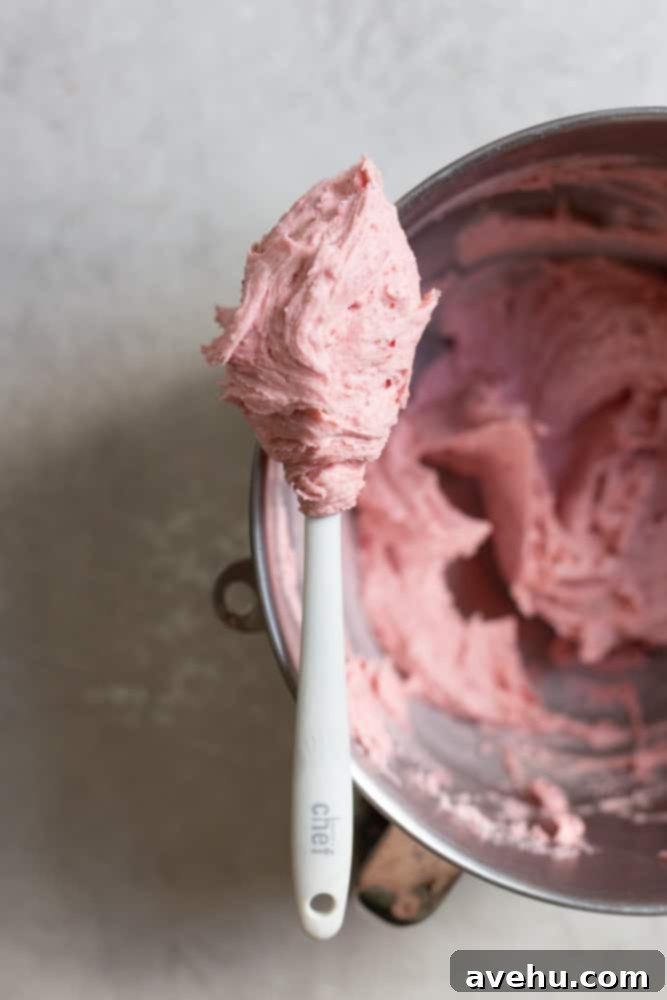 Aromatic Strawberry Basil Cake with Strawberry Buttercream 9 A vibrant strawberry pink buttercream, held aloft on a spatula, showcasing its smooth, airy, and luscious texture.