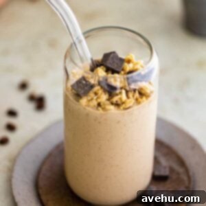 Blended Coffee Banana Boost 2 A glass cup filled with a creamy coffee banana smoothie, topped generously with crunchy granola and rich dark chocolate chunks.