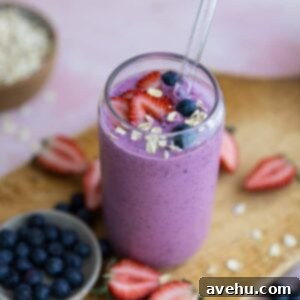 Berries and oats on top of a smoothie in a glass cup.
