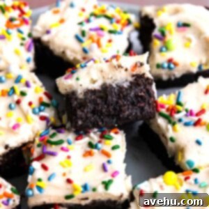 Birthday brownies stacked on top of each other on a plate with vanilla frosting and sprinkles.