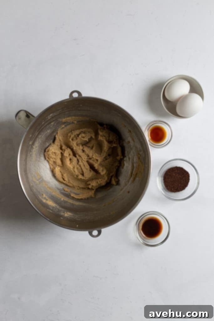 Coffee-Infused Chocolate Chip Chews 5 A stand mixer bowl with cookie batter inside. There are 4 small bowls next to it. One bowl has 2 eggs, another has vanilla extract, another has brewed coffee, and the last has coffee granules