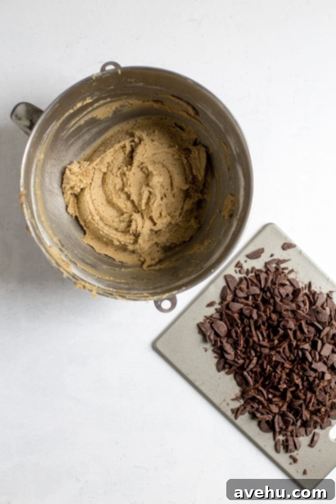 Coffee-Infused Chocolate Chip Chews 7 A stand mixing bowl with cookie batter inside next to a gray cutting board with chopped up chocolate on it.
