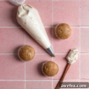 Achieve Perfect Frosting Consistency Instantly 2 A piping bag with frosting next to un-frosted cupcakes on a pink tiled surface.