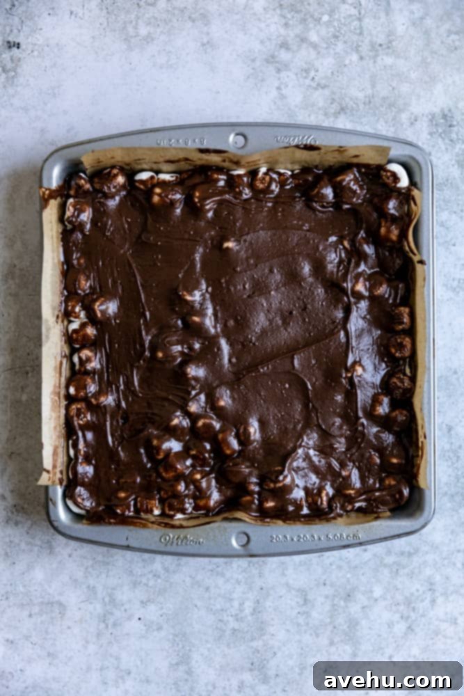 Ultimate Marshmallow Brownie Indulgence 3 Rich chocolate fudge frosting being spread over the toasted marshmallow layer on brownies in a baking pan.