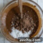 Dry ingredients added to brownie batter in a glass bowl.