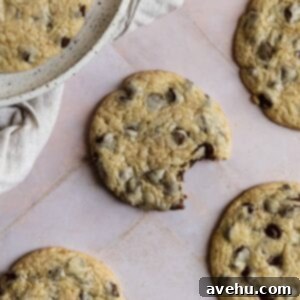 Simple Chocolate Chip Cookies No Brown Sugar Required 2 A chocolate chip cookie with a bite taken out on a pink tiled surface.
