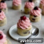 Effortless Cherry Frosting 5 A cherry cupcake with cherry frosting on a white plate garnished with a fresh cherry.