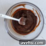 Instant Indulgence Brownie Bites 3 Melted chocolate in a glass bowl with a white spatula.