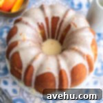 Zesty Citrus Bundt Bliss 8 An orange bundt cake with icing on a blue patterend surface.
