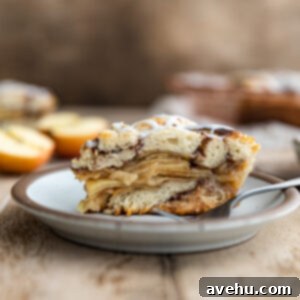Effortless Cinnamon Roll Apple Pie 2 A slice of cinnamon roll apple pie on a plate with a fork, showcasing its layers.