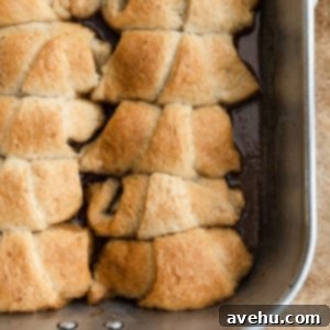 Buttery Flaky Apple Dumplings 2 Apple dumplings lined up and baked in a pan, showcasing their golden-brown crust and sweet sauce.
