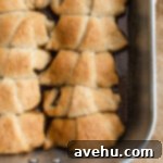 Buttery Flaky Apple Dumplings 6 Apple dumplings lined up and baked in a pan, showcasing their golden-brown crust and sweet sauce.