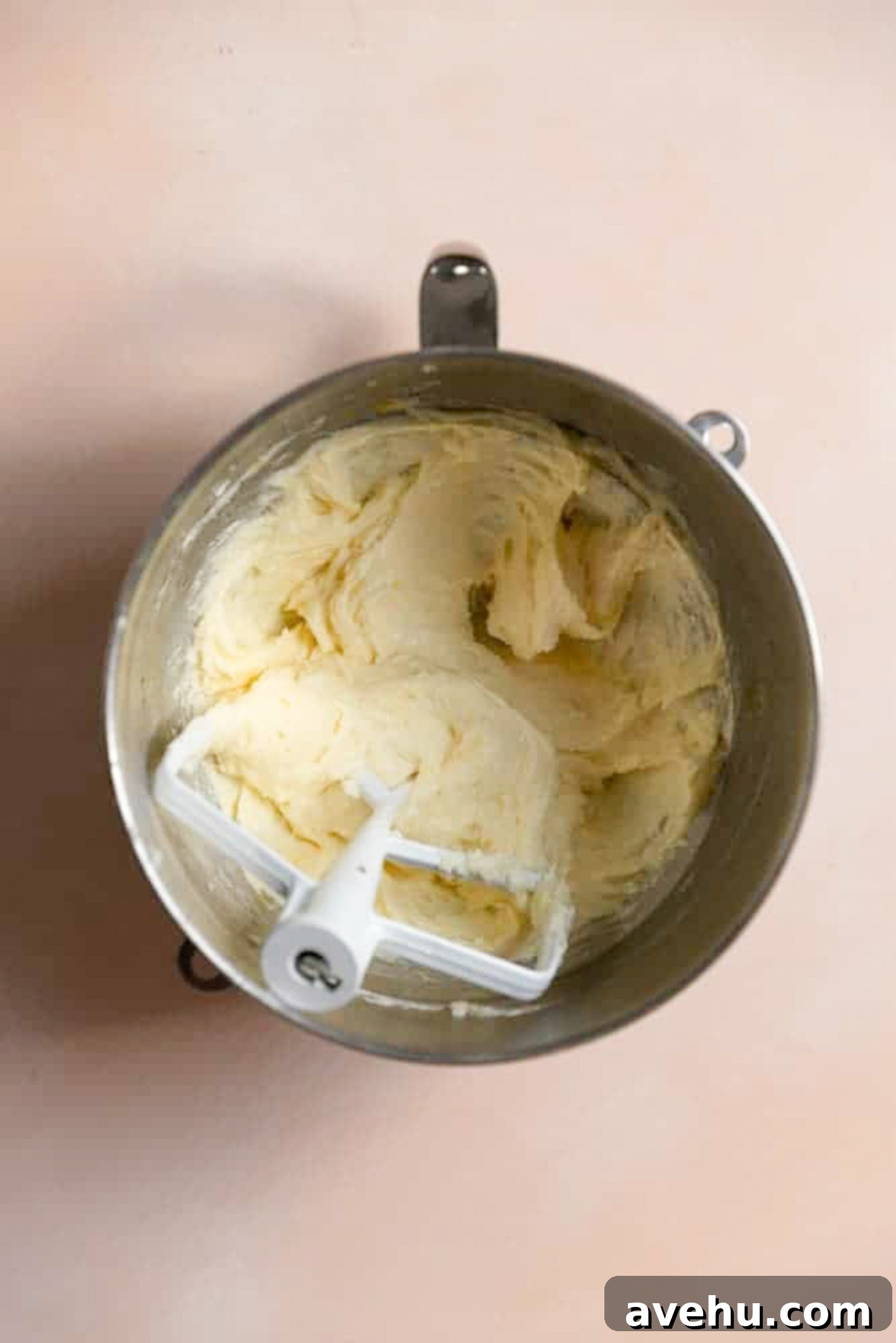 A mixture or butter, sugar, and eggs in a mixing bowl with a paddle attachment.