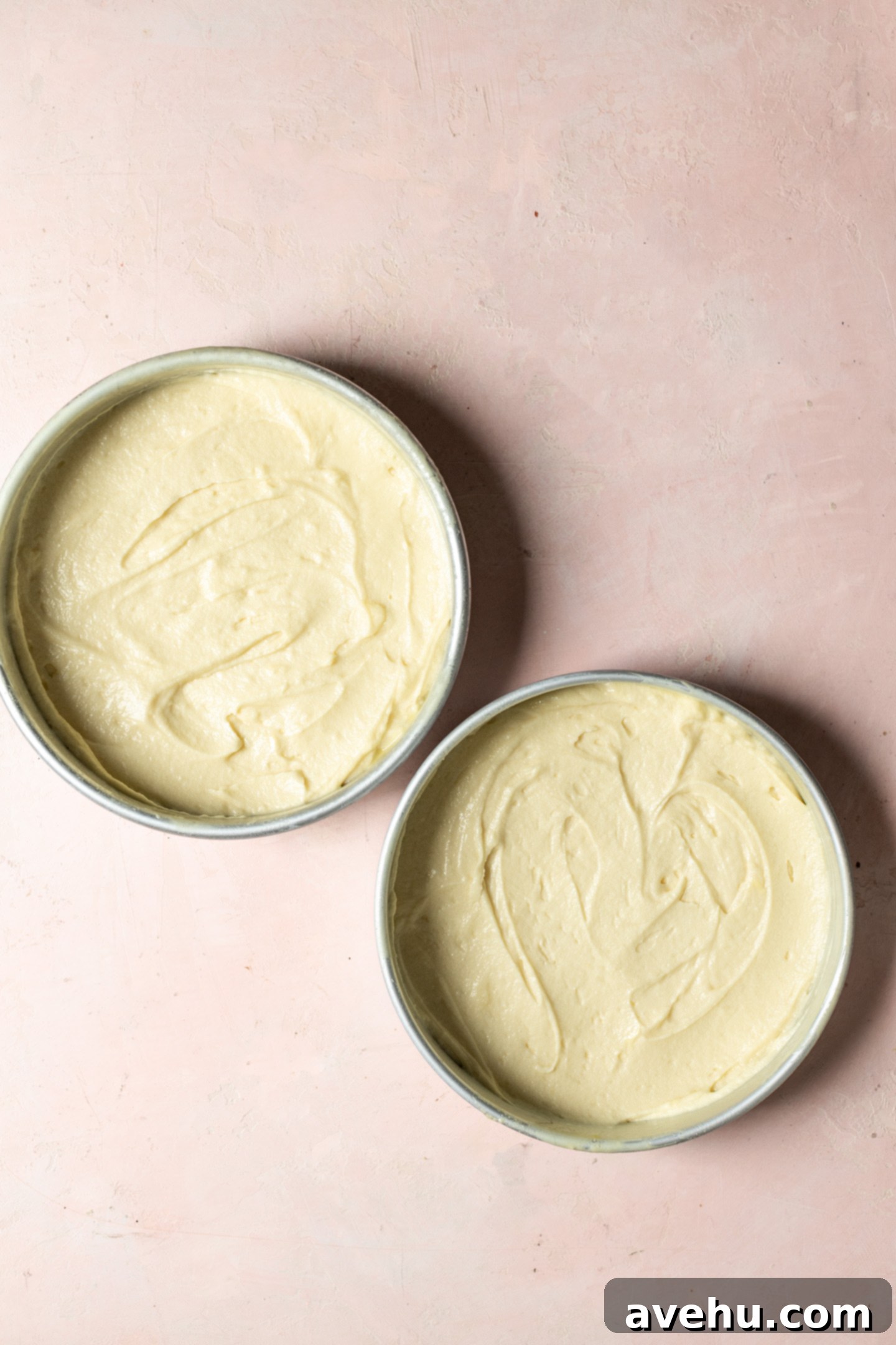 2 cake pans with yellow cake batter in it on a pink surface