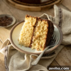 Golden Vanilla Cake with Silky Chocolate Buttercream 8 A slice of yellow cake with chocolate frosting on a rustic plate and linen napkin.