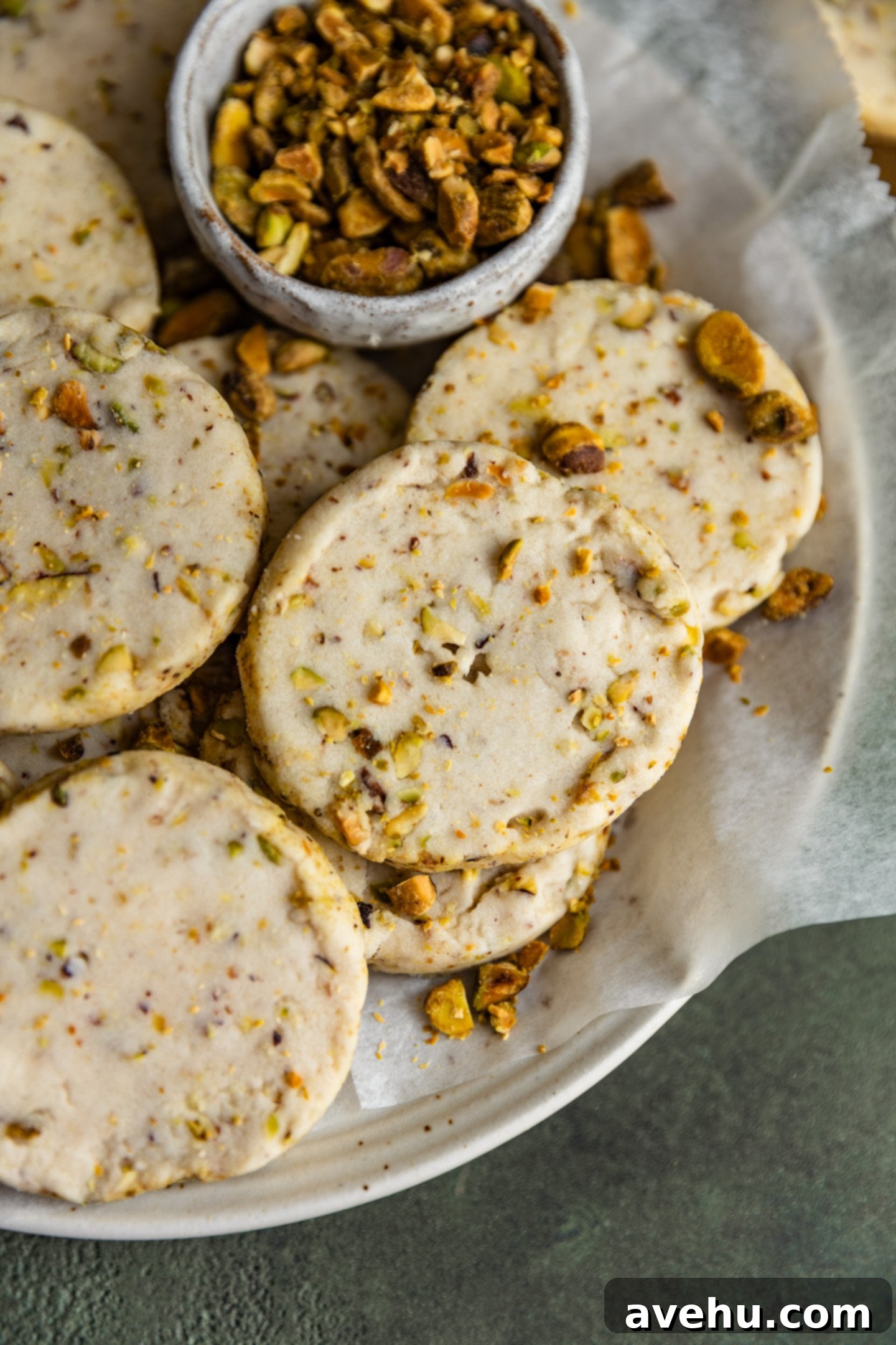 Buttery Pistachio Shortbread Logs 2 A stack of perfectly round pistachio shortbread cookies in a rustic bowl, with more cookies scattered around.