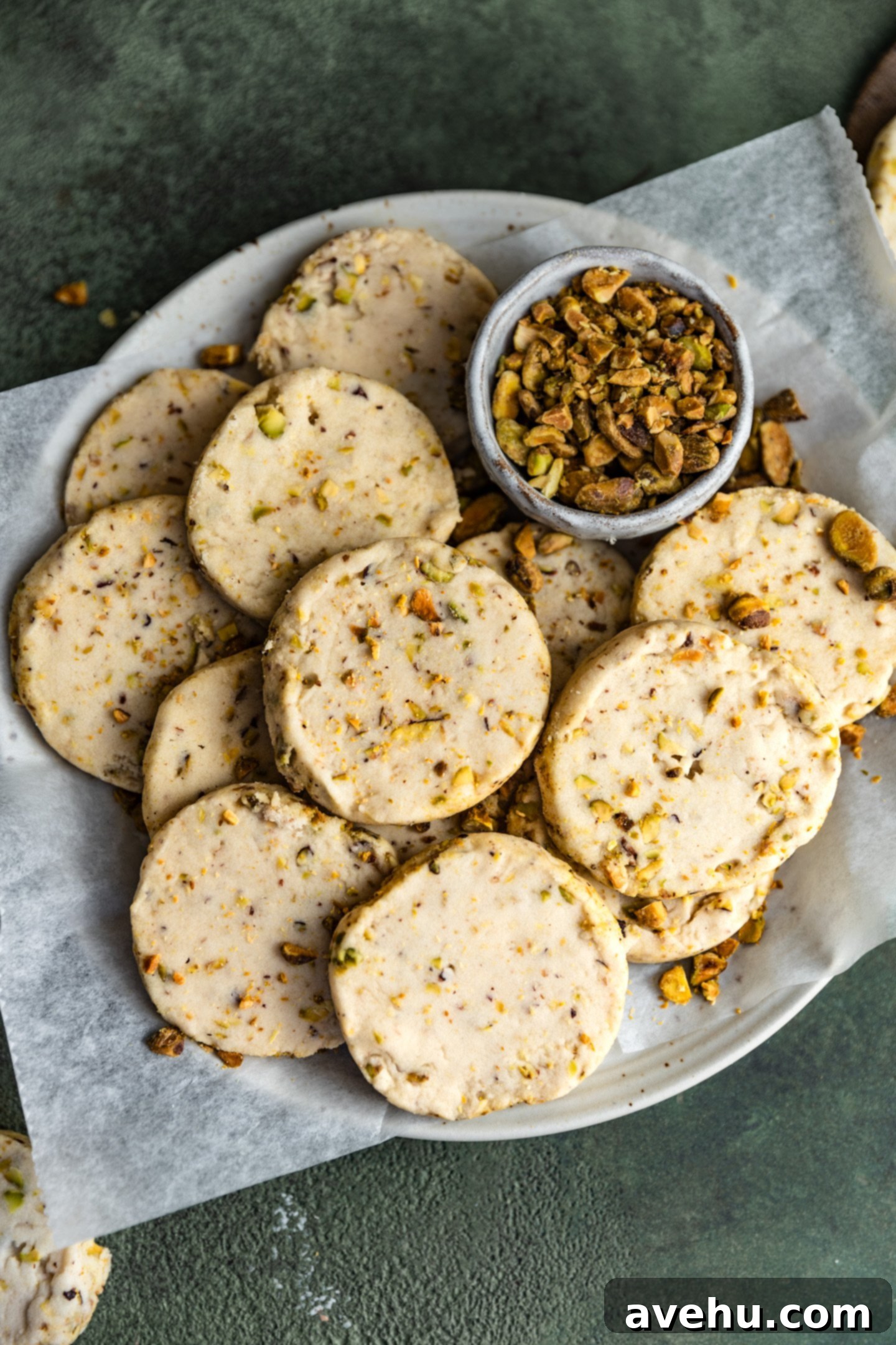 Buttery Pistachio Shortbread Logs 12 An inviting arrangement of perfectly round pistachio shortbread cookies, artfully lined in a bowl, accompanied by a small dish of chopped pistachios.