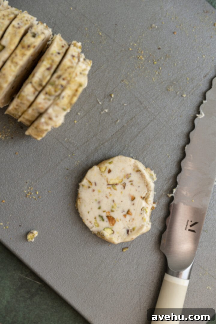 Buttery Pistachio Shortbread Logs 10 A single slice of pistachio shortbread dough neatly cut from the main log, showcasing its round shape and visible pistachios.