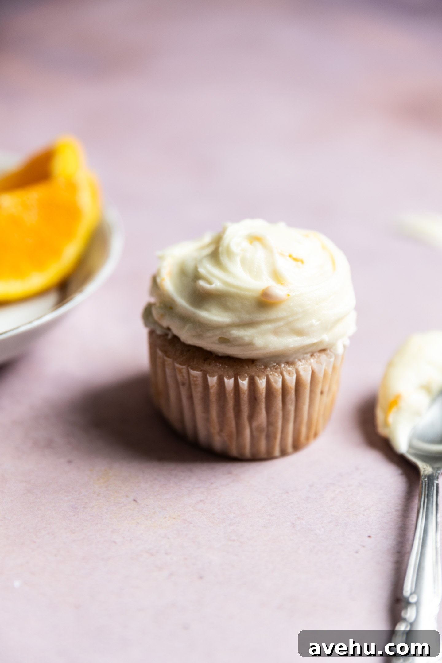 Orange Zest Cream Cheese Cloud 2 A cupcake topped with orange cream cheese frosting on top on a pink background.