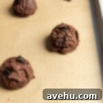Quick 25-Minute Double Chocolate Chip Cookies 4 A chocolate cookie dough ball on a cookie sheet lined with brown parchment paper.