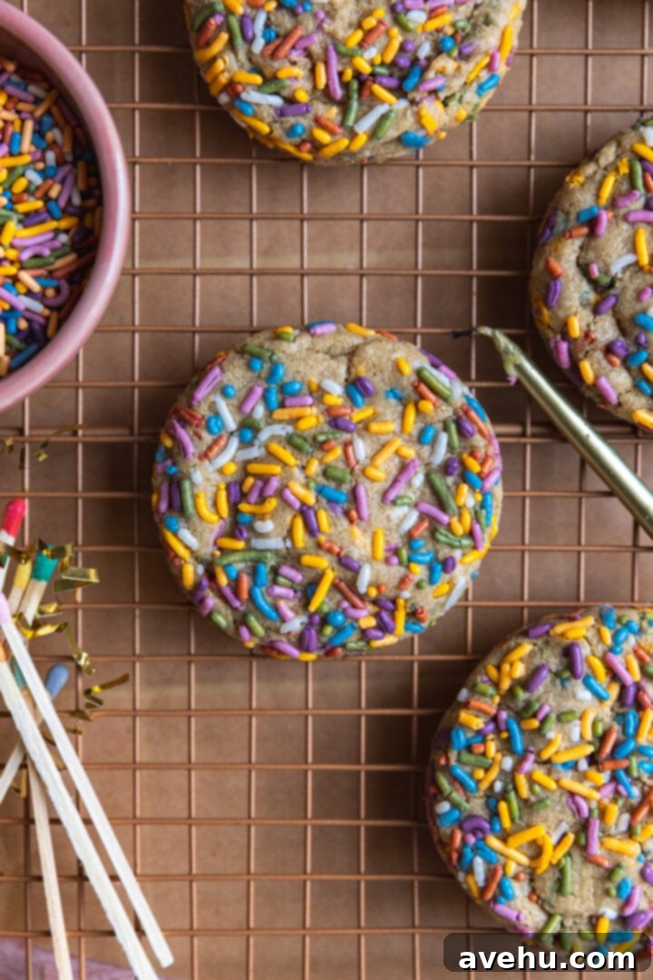 Quick 30 Minute Birthday Cake Cookies 2 A colorful sprinkle cookie on a cooling rack next to candles and matches, with more sprinkles in a bowl.
