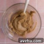 Unfinished cookie batter in a glass bowl and spatula.