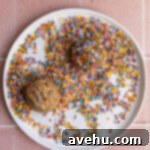 Cookie dough balls rolled in colorful sprinkles on a white plate.