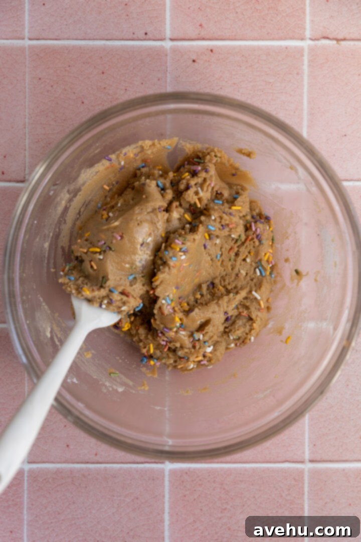 Quick 30 Minute Birthday Cake Cookies 5 Birthday cake cookie batter in a glass bowl with sprinkles gently folded in, maintaining their vibrant shape.