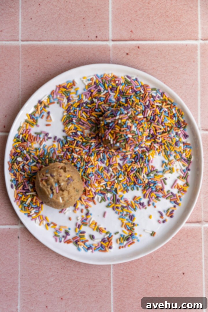 Quick 30 Minute Birthday Cake Cookies 6 Cookie dough balls rolled thoroughly in colorful sprinkles on a white plate, ready for baking.