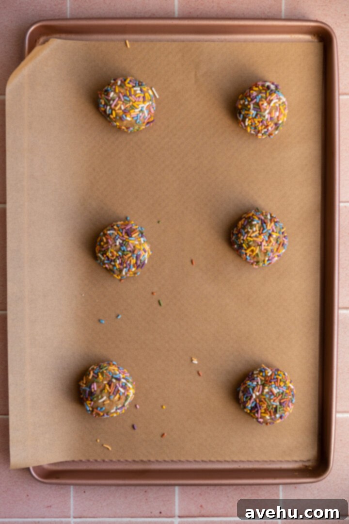 Quick 30 Minute Birthday Cake Cookies 7 Birthday cake cookie dough balls, generously coated in sprinkles, neatly lined on a baking sheet, spaced for even baking.