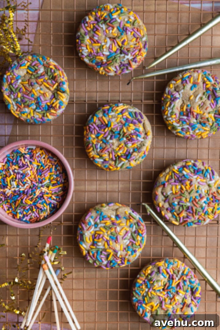 Quick 30 Minute Birthday Cake Cookies 8 Birthday cake cookies cooling on a wire rack next to a bowl of vibrant jimmy sprinkles, festive candles, and matches.