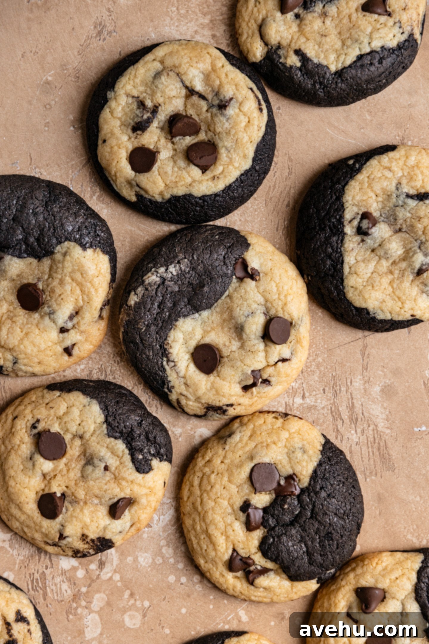 A close-up of a batch of freshly baked, perfectly rounded brookies cookies cooling on a beige surface, each showcasing its unique swirl of brownie and chocolate chip dough.