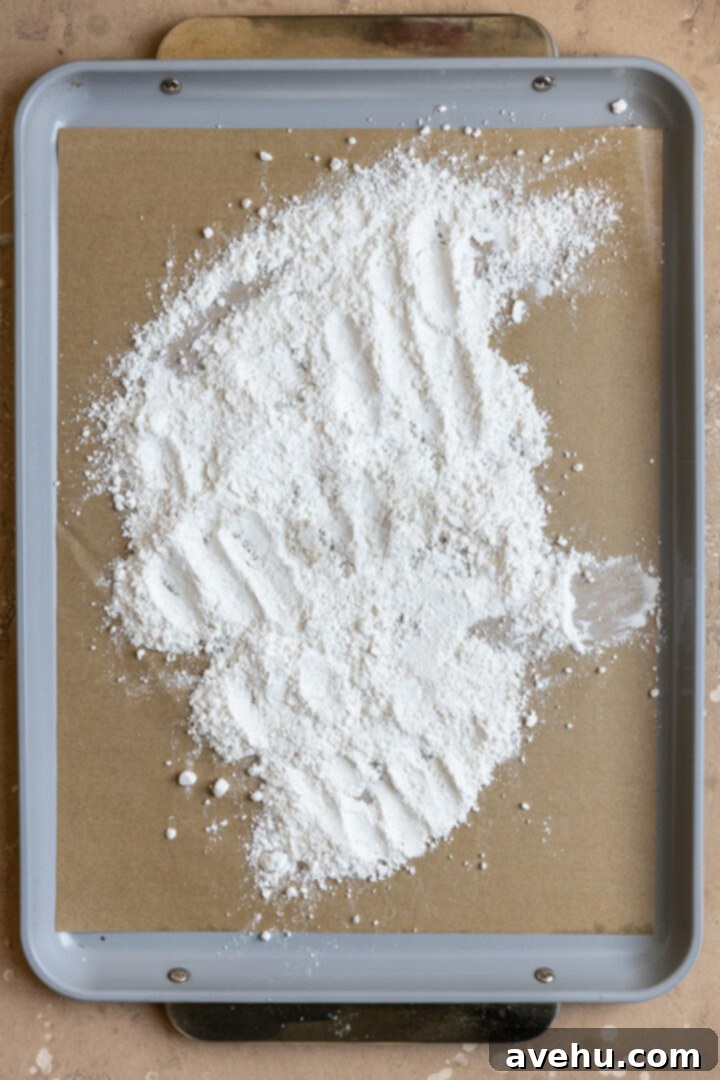 Silky Smooth Cookie Dough Frosting 3 All-purpose flour spread thinly and evenly on a parchment-lined baking tray, ready for heat treatment in the oven.