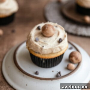 Silky Smooth Cookie Dough Frosting 10 A cookie dough cupcake on an upside down plate on a brown surface, topped with edible cookie dough frosting and mini chocolate chips.