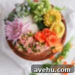 Elegant Floral Cake Designs Made Easy 4 A white cake on a brown cake stand decorated with a rainbow of fresh flowers, illustrating elegant floral cake design.