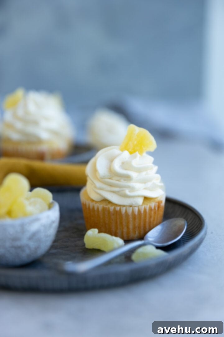 Effortlessly Moist Pineapple Cupcakes 2 A pineapple cupcake garnished with candied pineapple on a blue plate next to a resting spoon.