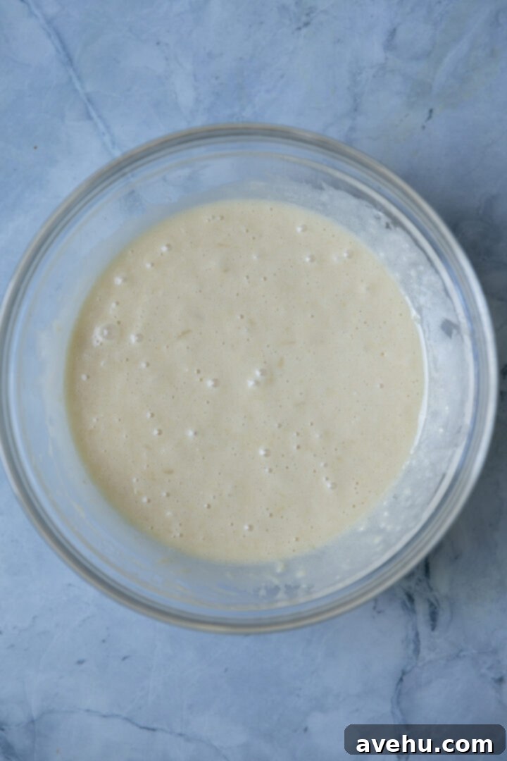 Effortlessly Moist Pineapple Cupcakes 5 Cupcake batter in a glass bowl on a blue surface.