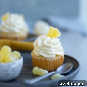 A pineapple cupcake garnished with candied pineapple on a blue plate next to a resting spoon.